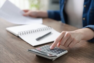 Budget. Woman with paperwork and calculator at wooden desk indoors, closeup