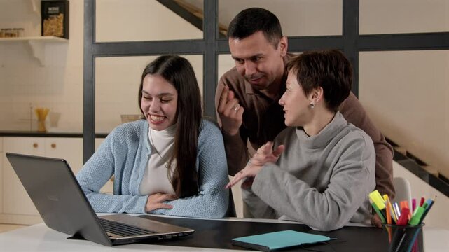 Positive attractive hearing impaired parents and pretty teenage daughter with hearing loss making video call online on laptop, communicating and sharing with relatives using sign language indoors.