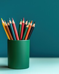 Fototapeta premium A vibrant collection of colored pencils arranged in a green holder against a teal background, showcasing creativity and artistic potential.