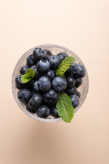 View from above of a glass cup filled with fresh blueberries with mint leaves on beige background. Copy Space. Concept of nutrition, freshness and healthy cooking