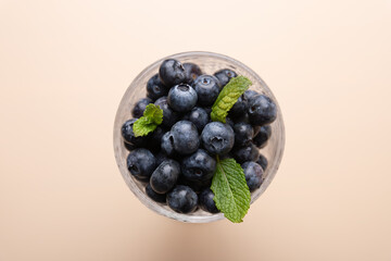 View from above of blueberries in a glass with mint leaves on a beige background. Copy Space. Fruit and healthy eating concept