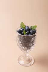 Fresh blueberries in crystal glass with cut details, decorated with mint leaves on neutral background. Copy Space. Minimalist composition. Concept of freshness, healthy eating and elegance