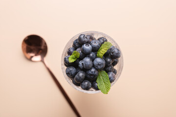 View from above of a glass cup filled with fresh blueberries, mint leaves and copper spoon on neutral background. Copy Space. Concept of nutrition, freshness and healthy cooking