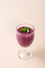Blueberry milkshake in cut crystal glass, decorated with mint leaves on neutral background. Elegant and minimalist presentation. Copy Space. Concept of healthy eating, freshness and wellness