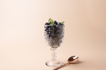 Blueberries in glass cup decorated with mint leaves and copper spoon on soft background. Delicate lighting. Copy Space. Concept of freshness, wellness and natural food