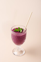 Purple milkshake in glass cup with beige straw and mint, on neutral background. Harmonious and aesthetic composition. Copy Space. Concept of healthy eating, antioxidants and wellness