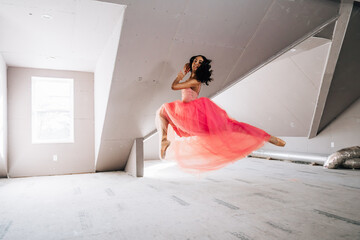 Ballerina in mid-air leap wearing pink tulle dress in bright loft