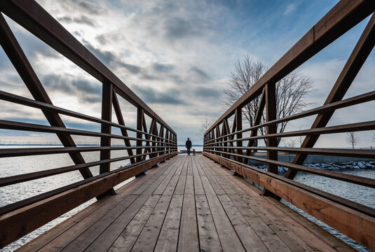 Low angle of man walking dog across bridge on winter day.
