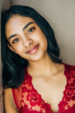 Teen in red lace dress leaning on wall, soft smile, natural light