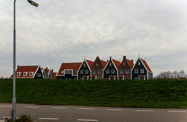 Traditional Dutch-style houses with steep gabled roofs lined up behind lush green dike under cloudy...