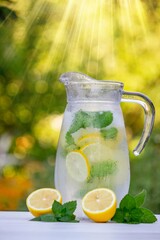 Glass of lemonade with lemons and fresh mint, on a light background in the garden.