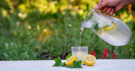 Glass of lemonade with lemons and fresh mint, on a light background in the garden.