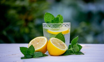 Glass of lemonade with lemons and fresh mint, on a light background in the garden.
