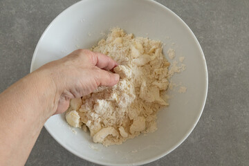 A hand mixes the butter pieces with the flour.