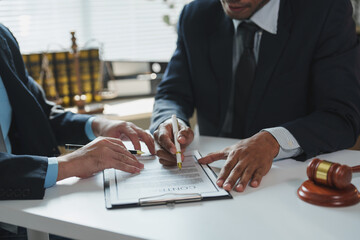 Two male lawyers in suits are sitting at a white table, carefully reviewing and discussing contract...
