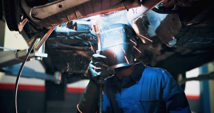 Mechanic, helmet and welding on car for maintenance, repairs and problem solving in workshop. Man, engineer and blowtorch in auto garage for vehicle service, sparks and industrial work with safety
