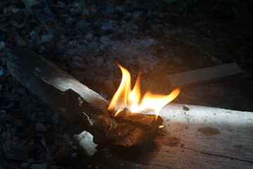 Bright flames ignite on a wooden base among scattered stones, highlighting the charm of fire in the dark.