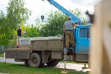 A man unloads paving stones on pallets with a truck crane