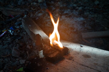 Bright flames ignite on a wooden base among scattered stones, highlighting the charm of fire in the...