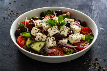 Greek style salad - fresh vegetables with feta cheese, kalamata olives on black table