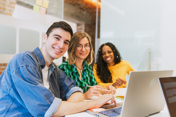 Multicultural team of young entrepreneurs working together in a coworking office, smiling and using laptops. Concept of diversity, teamwork, and innovation.