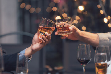 Cheers to Connection: A toast to friendship, camaraderie, and celebration. Two hands raise glasses of amber liquid in a warm and intimate moment, captured in a dimly lit setting.  