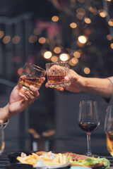 Toasting to Good Times: Two hands clink glasses of amber liquor in a cozy, dimly lit bar setting, the warm glow of fairy lights casting a magical ambience. Cheers to friendship, camaraderie.