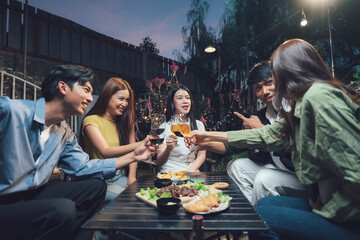 Nighttime Backyard Gathering: Friends enjoying a lively evening, clinking glasses and sharing laughter around a table filled with food and drinks in a cozy backyard setting. 