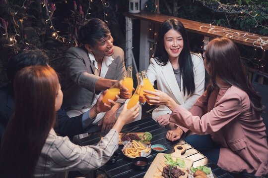 Cheers to Good Times: A group of friends gather around a table on a patio, raising their glasses in a celebratory toast. Warm lighting and lush greenery create a convivial ambiance.