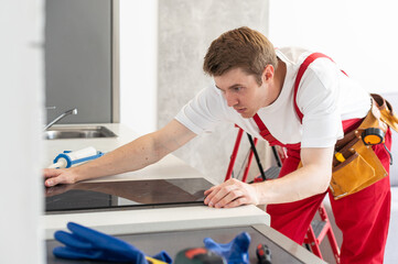 Gloved craftsman installs hob in kitchen. Household Appliance Installation Services Concept