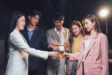 Cheers to the Night: A group of friends raise their glasses in a toast, their smiles radiant under the warm glow of outdoor lighting, creating a vibrant and celebratory atmosphere.