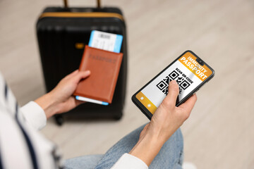 Tourist with passport, flight ticket and mobile phone indoors, above view. Immunity passport app with QR code on device screen