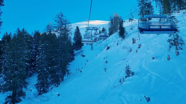 A ski chairlift glides through a shadowy valley, carrying passengers to the Metschstand top station in the Adelboden-Lenk ski region on a crisp winter morning