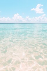 Clear turquoise water reflects the bright sky over a serene beach at midday under soft, fluffy clouds