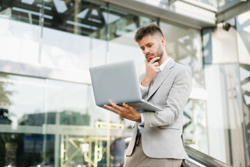 Fototapeta premium Handsome unshaven businessman walking with laptop, tablet and smartphone on city