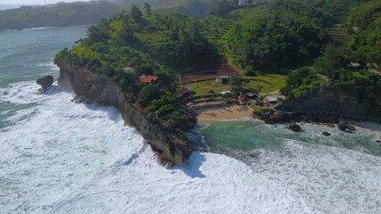 Aerial Drone view of the beach with white sand, coral rocks, hills with trees, waves from the ocean which is a tourist destination known as Mbuluk Beach Gunung Kidul Yogyakarta