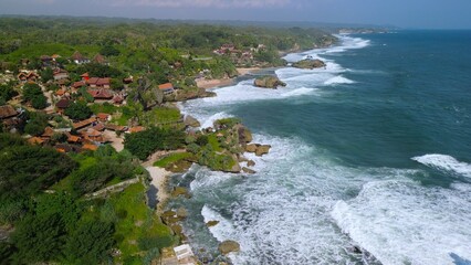 Aerial Drone view of the beach with white sand, coral rocks, hills with trees, waves from the ocean which is a tourist destination known as Mbuluk Beach Gunung Kidul Yogyakarta
