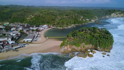 Aerial Drone view of the beach with white sand, coral rocks, hills with trees, waves from the ocean which is a tourist destination known as Drini Beach Gunung Kidul Yogyakarta