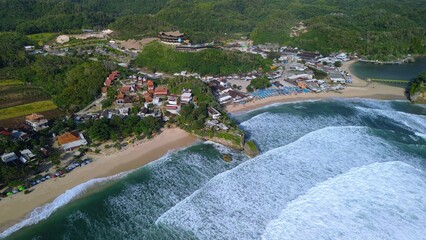 Aerial Drone view of the beach with white sand, coral rocks, hills with trees, waves from the ocean which is a tourist destination known as Drini Beach Gunung Kidul Yogyakarta