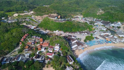 Aerial Drone view of the beach with white sand, coral rocks, hills with trees, waves from the ocean which is a tourist destination known as Drini Beach Gunung Kidul Yogyakarta