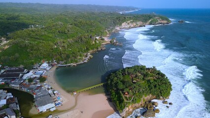 Aerial Drone view of the beach with white sand, coral rocks, hills with trees, waves from the ocean which is a tourist destination known as Drini Beach Gunung Kidul Yogyakarta