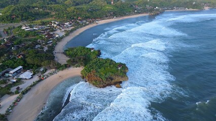 Aerial Drone view of the beach with white sand, coral rocks, hills with trees, waves from the ocean which is a tourist destination known as Krakal Beach Gunung Kidul Yogyakarta