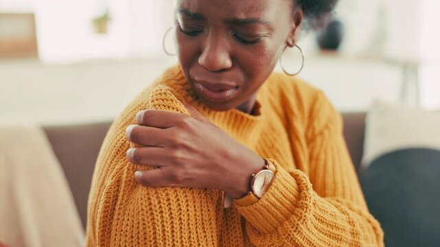Home, sore and woman with shoulder pain, injury and massage for inflammation in living room and sofa. House, hurt and black person with fracture on arm, joint and girl with muscle tension in lounge