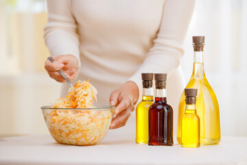 Woman hold glasses bottle with fresh extra virgin, sunflower oil pouring into bowl of vegetable...