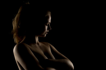 Naklejka premium Low-key portrait of a blonde woman with head tilted back. Dramatic side lighting accentuates neck, shoulders, and arms. Silhouette effect against dark background