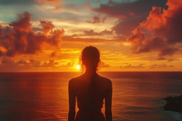 Silhouette of a woman facing a breathtaking ocean sunset, vibrant colors fill the sky.