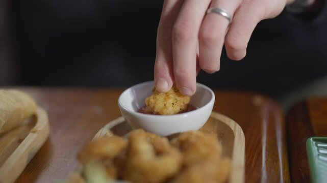 A person is eating a piece of chicken nugget with a dipping sauce. The image conveys a casual and relaxed atmosphere, as the person is enjoying their meal in a comfortable setting