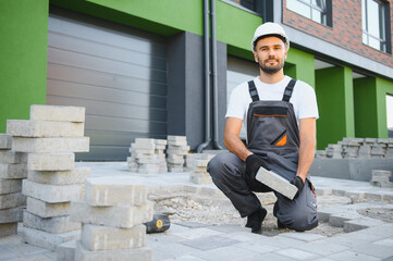 Worker skillfully laying paving stones using a hammer and wearing gloves, showcasing precision
