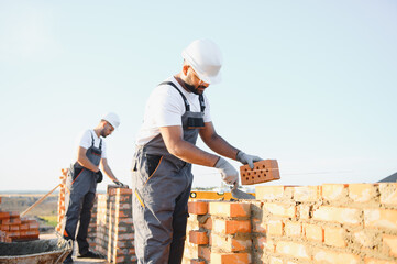 A team of Indian construction workers in overalls and hard hats are building a brick wall