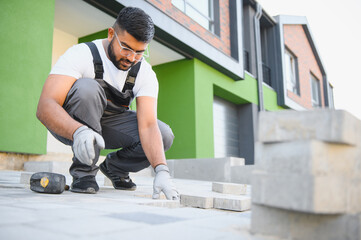 Indian worker lay paving tiles, construction of brick pavement, men's hands in gloves.